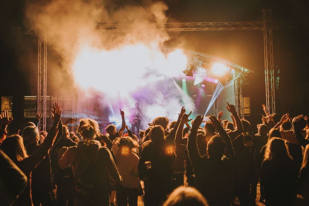 Feiernde Menschen jubeln im Dunkeln vor einer bunt beleuchtetenden Bühne in Nebelwolken